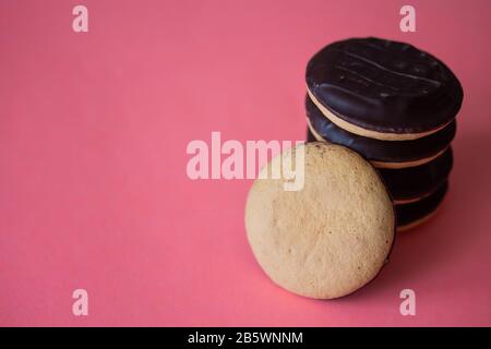 A pile of Jaffa cakes. Cookies covered with dark chocolate and filled with pink strawberry or cherry marmalade. Delicious biscuits isolated on pink background with copyspace Stock Photo