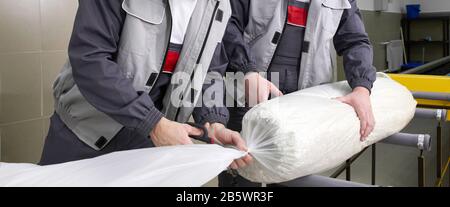 Men workers packing carpet in a plastic bag after cleaning it in automatic washing machine and dryer in the Laundry service Stock Photo