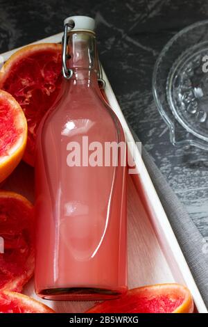 Freshly squeezed grapefruit juice in a glass bottle, a juicer and fruit peels on a concrete background. Stock Photo
