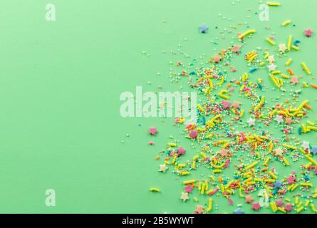 Sprinkle background with multicolored cake topping sprinkles scattered on pale green backdrop with space for text Stock Photo