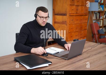 concentrated man in headphones using laptop while sitting over grey background Stock Photo