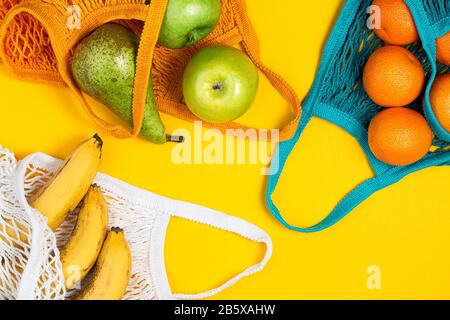 Tangerines, banana and green apples in string bag on yellow background. Zero waste, plastic free concept. Healthy clean eating diet and detox. Summer Stock Photo