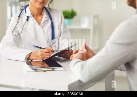 Female doctor therapist gross allergist nutritionist otolaryngologist and male patient sitting at a table in a clinic office Stock Photo