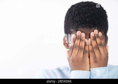 Unhappy Boy Covering Face With Hands Against White Background Stock Photo