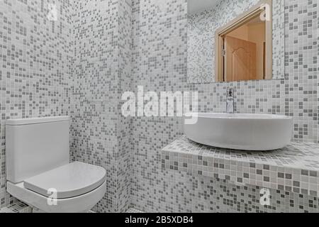 Toilet bowl in the bathroom. Restroom with grey mosaic walls and sink Stock Photo