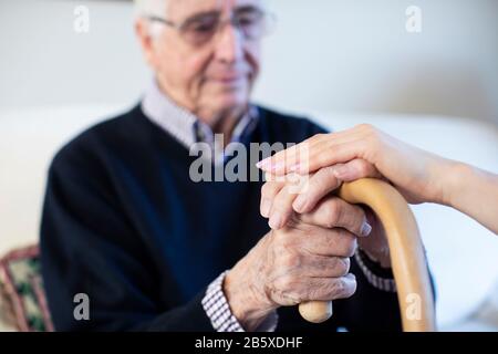 Unhappy Senior Man With Hands On Walking Stick Being Comforted By Woman Health Visitor Stock Photo