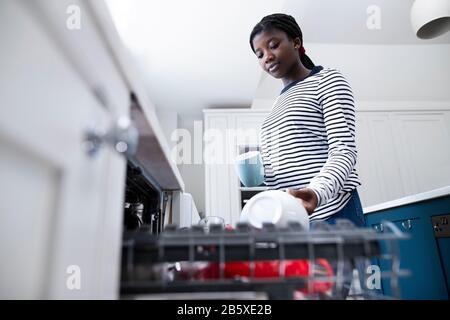 Teenage Girl Boy Helping With Chores At Home By Stacking Crockery In Dishwasher Stock Photo