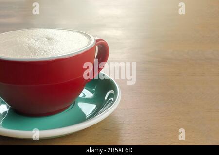 A cup of cappuccino, raf coffee, on wooden background. Red ceramic cup and greenery saucer. Stock Photo
