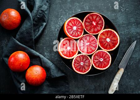Cutted blood oranges in a plate on a black background. Stock Photo