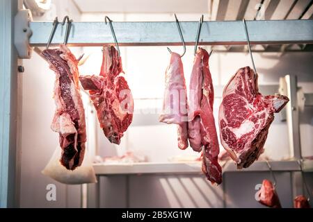 Pieces of fresh beef meet hanging on metal hooks in butchery refrigerator room, viewed from low angle Stock Photo