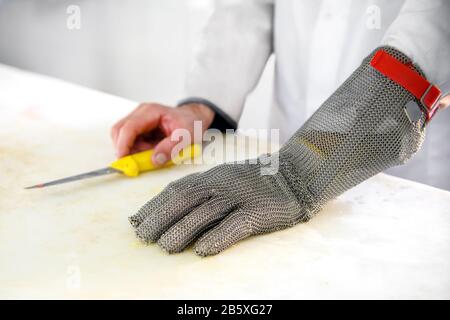 Close up on a chain mail butchers protective glove with metal mesh to prevent cuts from knives on the hand of a male butcher resting on a cutting boar Stock Photo