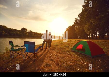 A hiker couple hugging next to a tent by the lake at sunset.