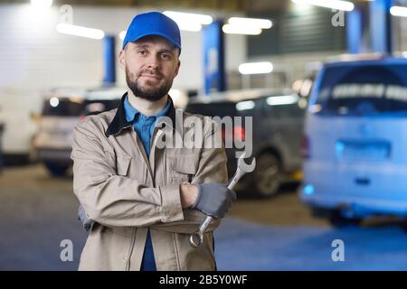 Horizontal waist up portrait of mature Caucasian auto mechanic standing with arms crossed holding spanner looking at camera, copy space Stock Photo