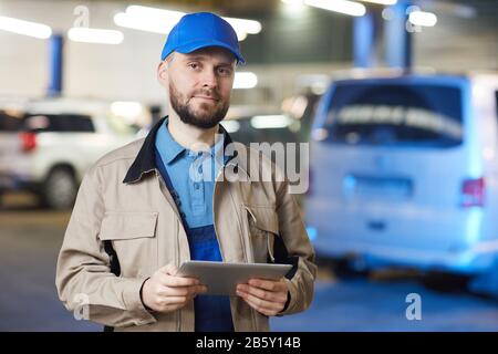 Horizontal waist up portrait of mature Caucasian auto mechanic holding tablet PC looking at camera, copy space Stock Photo