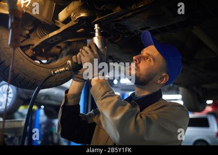 Horizontal medium close up shot of mature Caucasian repairman with beard in face working under car Stock Photo