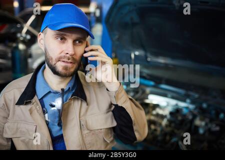 Horizontal chest up portrait of mature Caucasian repairman talking on phone while having break, copy space Stock Photo