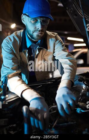Vertical shot of mature Caucasian auto service specialist wearing protective uniform and eyewear fixing modern car engine parts Stock Photo