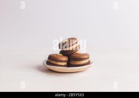 Tasty french macarons on a plate. White background. Chocolate macarons with peanuts. Place for text. Stock Photo
