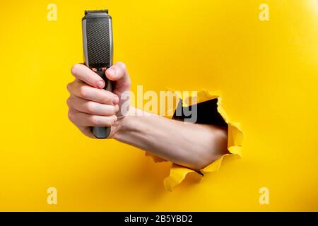 Hand holding a shaver through torn yellow paper background Stock Photo