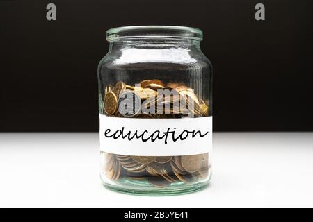 Coins in a jar with education text on a white label. Savings abstract concept. Copy space. Stock Photo