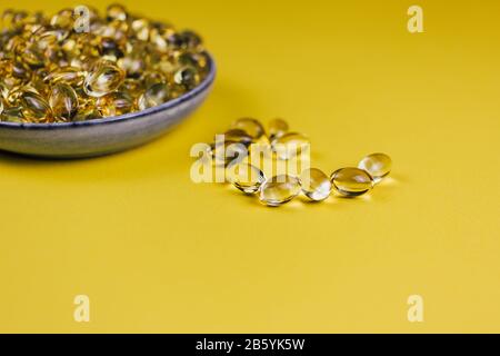 capsules filled with omega 3 fish oil fatty acids lay in a heap on an yellow background, concept of health care and cardiovascular system. Stock Photo