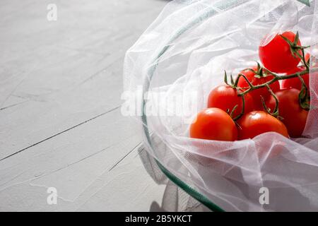 The reusable organza net bag for shopping with tomatoes a grey background.  Concept of no plastic, zero waste, reusable life. Copy space. Stock Photo