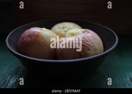 Oven-baked apples stuffed with ricotta in ceramic bowl on dark wooden background. Healthy fruit dessert Stock Photo