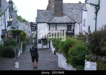Male Hiker Walking down Steep Cobbles to the New Inn Hotel in the Fishing Village of Clovelly on the South West Coast Path, North Devon. England, UK. Stock Photo