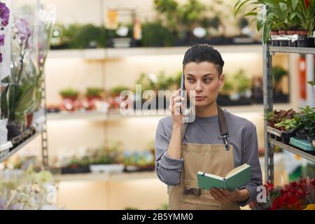 Portrait of successful female business owner speaking by smartphone while standing in flower shop, copy space Stock Photo