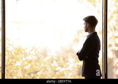 Concentrated thoughtful young businessman looking away at panoramic office window. Stock Photo