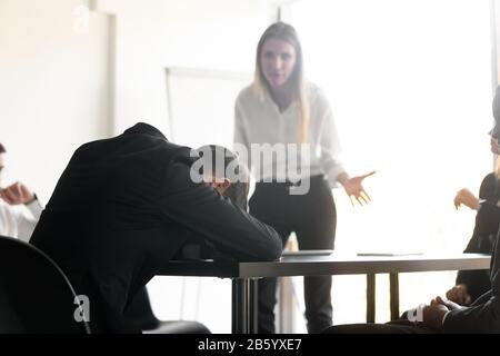 Angry disappointed female team leader boss looking at tired employee. Stock Photo