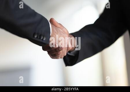 Two mixed race businessmen in suits shaking hands at office. Stock Photo