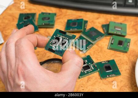 a human hand holds a microprocessor from a computer against the background of a table and a lying pile of other processors Stock Photo