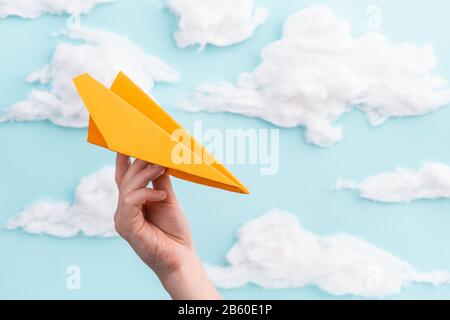 Orange paper airplane in child's hand flying on blue sky background Stock Photo