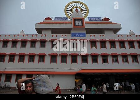 An unidentified man carries a loaded sack with Varanasi Junction railway station in the background. Stock Photo