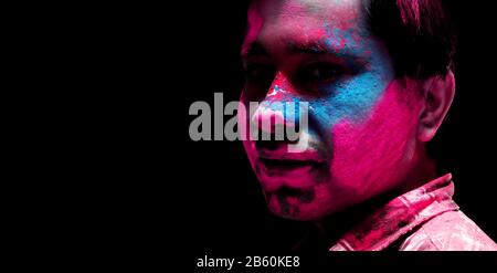 Closeup shot of Indian young man covered with multi color dry paint with copy space in black background at Holi Festival