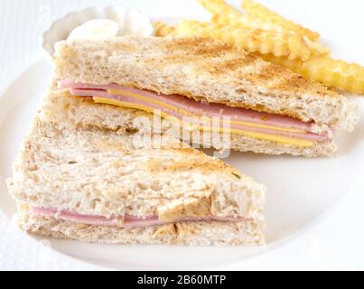 Ham and cheese sandwich and French fries with mayonnaise sauce on white plate on wood table at restaurant. Stock Photo