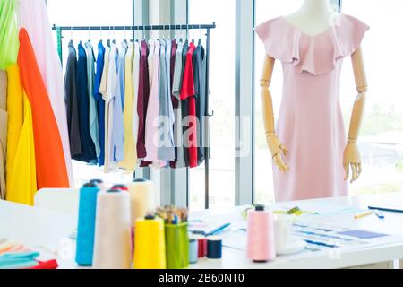 Fashion designer working desk with colorful sewing thread, colored pencils and fabric sample including mannequin and hanging clothes at the office or Stock Photo