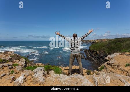 Tourist man on the rocky shore of the sea. He opened his arms with happiness. Stock Photo