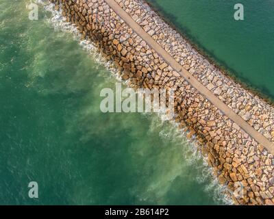 Aerial. Industrial breakwater, washed the waves in the sea. Filmed from the sky. Stock Photo