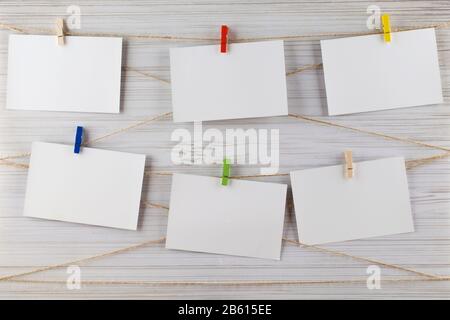 Empty colored paper sheets for notes, frames that hang on a rope with clothespins on white background. Blank cards on rope mockup template. Stock Photo