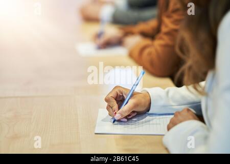 Picture of a human hand writing something on the paper on the foreground Stock Photo