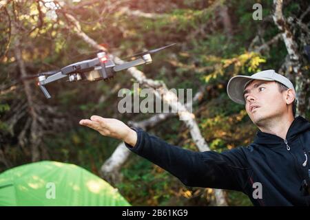 A man in a camping on the background of a tent launches a flying drone for taking photos and video Stock Photo