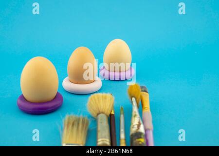 Easter eggs coloring concept with three unpainted eggs and set of different paint brushes, on blue background Stock Photo
