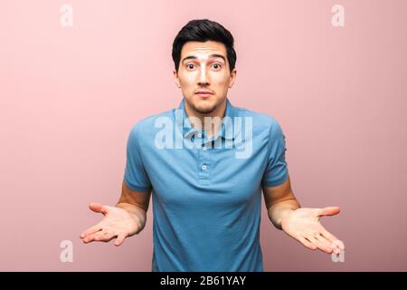 handsome man in blue polo shirt asking gesture against pink background. what is wrong Stock Photo