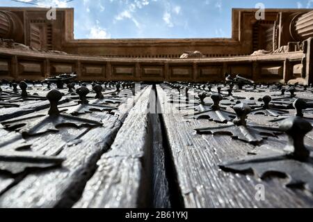 detail of the ornaments and engravings of wooden main door of a church seen from below with the blue sky and part of the stone lintel Stock Photo