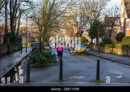 London, England, UK - January 17, 2020: Cyclists ride along residential streets that make up the Quietway 2 cycleway route in Hackney, past bollards t Stock Photo