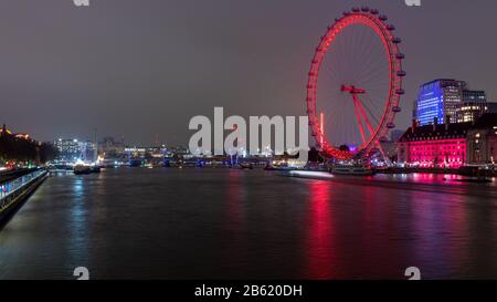 London, England, UK - November 21, 2019: The London Eye and bridges of the River Thames are lit at night in central London. Stock Photo