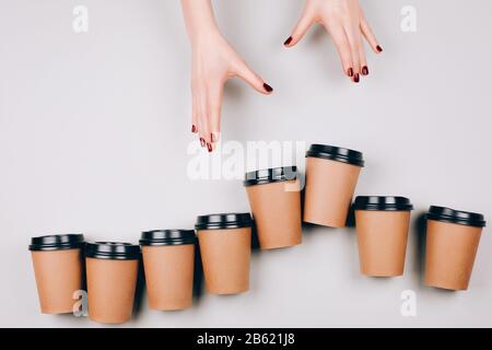 Beautiful hands follow to cardboard cups on pastel background. Concept of coffee addiction. Flat lay style. Stock Photo