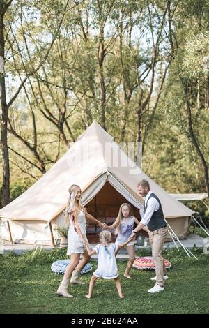 Family, leisure, holidays and people concept. Happy beautiful family with children dancing and having fun at summer in garden, boho wigwam tent on the Stock Photo